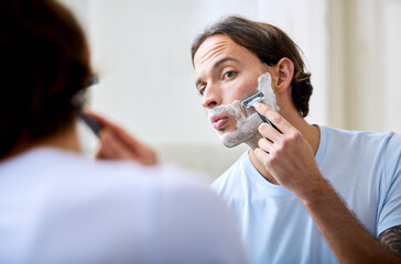 Man shave face in mirror, foam and beauty with morning routine, cosmetic care and grooming at home....