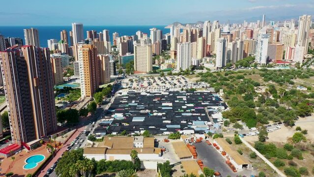 Aerial drone footage of the beautiful city of Benidorm in Spain in the summer time showing the famous outdoor outside market along side high rise apartments,