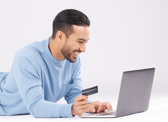Laptop, credit card and happy asian man on studio floor for ecommerce, sale or cashback on grey background. Online shopping, deal and Japanese male customer smile for loan, payment or sign up promo