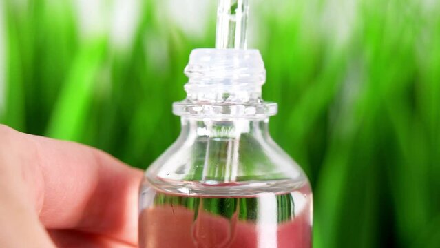 Extreme close up oil Bottle with a cosmetic pipette. glass bottle macro close-up isolated with green grass background.female hands takes a droplet of essential oil