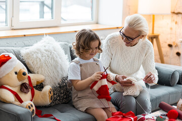 Grandmother and granddaughter spend quality time together, knitting, preparing handmade decoration...