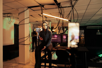 Hacker with mask breaking into computer system, attacking database and asking for ransom. Filming live broadcasting video stealing information, programming online malware at night.