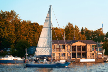The sailing yacht leaves the bay at sunset. The blue sailboat sets sail.