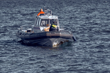 Rescuers on a rigid inflatable boat are on duty at sea. A small search and rescue ship with people...