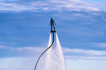 A man hovered in the air on a flyboard high in the sky. An athlete in water jet boots performs tricks in flight against the background of clouds. Male doing extreme sports