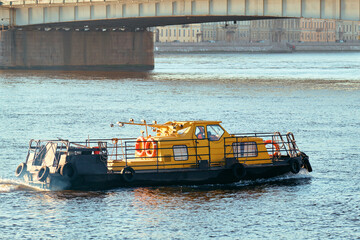 A yellow tugboat floats under the road bridge of a European city, close-up.