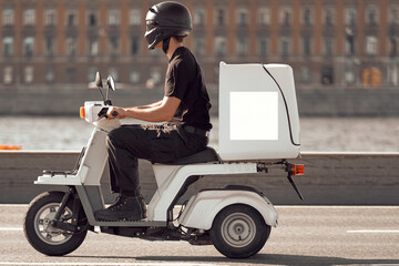 A man on a white electric scooter is in a hurry to complete the order. The courier carries the...