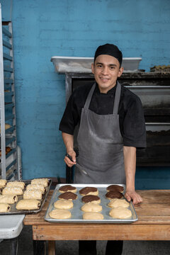 Un joven panadero Hispano sonriendo a c&aacute;mara mientras prepara conchas mexicanas