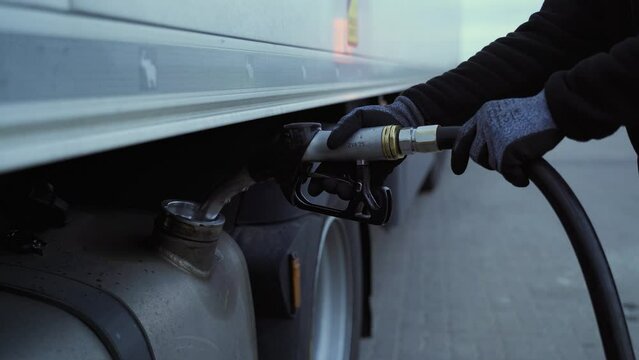 Refueling a truck with diesel fuel at a gas station. A close-up of the fuel tank and the driver's hands with a refueling gun.