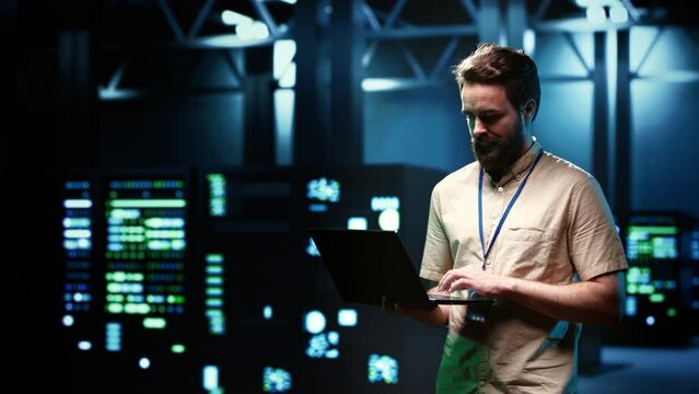 Electrician doing routine system probing, imputing data on tablet of required refurbishing in server rows housing advanced data storage equipment supporting critical IT workloads