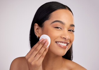 Happy woman, cotton pad and cleaning face in skincare for makeup removal against a grey studio...