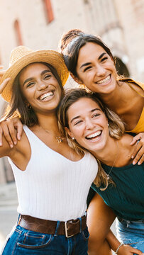 Vertical shot of multiethnic group of three happy young women having fun on summer vacation. Diverse female friends laughing together during their holidays. Female friendship concept.