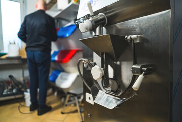 Detail of ice cream making machine with cook in black uniform in background. Stainless steel professional pastry machinery. High quality photo