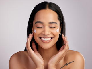 Happy woman, face and smile with cream for skincare, beauty or cosmetics against a grey studio...