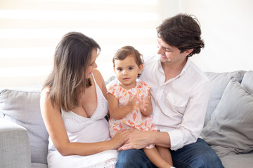 Smiling happy family with the father carrying their little daughter on his lap and pregnant mother