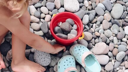 Cute little girl playing with stones on the beach putting them into bucket 