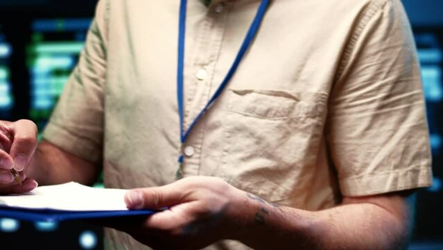 System admin doing maintenance, writing checklist of needed repairments in server farm housing advanced data storage infrastructure supporting critical IT workloads, close up