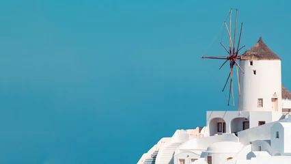 Fototapeten View of a Santorini hill and old traditional windmill on copy-space blue sky. © Carterson