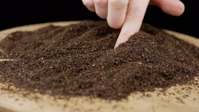 Woman Touching Dry Black Tea Granules with Finger on Rotating Wooden Background. Close up. Black background. Scattered heap of dry tea leaves on the surface. Texture. Plate. Particle, granular. Spin.