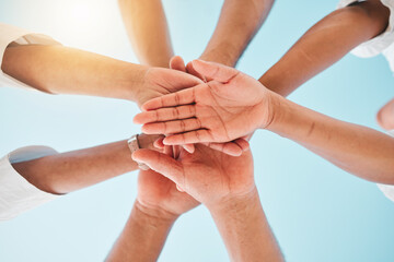 Circle, low angle and team with hands together for collaboration, unity or support by a blue sky....