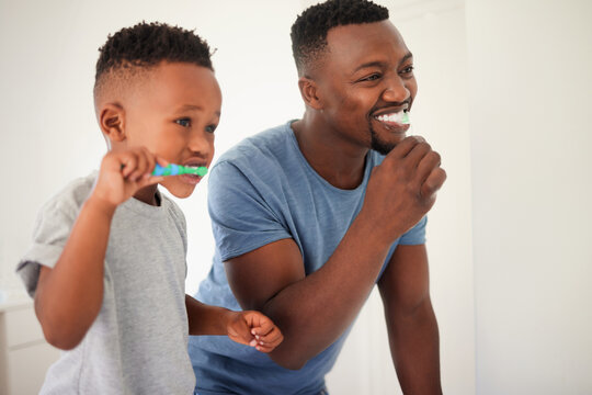 Father brushing his teeth with his child for oral hygiene, health and wellness in the bathroom. Dental, teaching and young African man doing his morning mouth routine with his boy kid at their home.