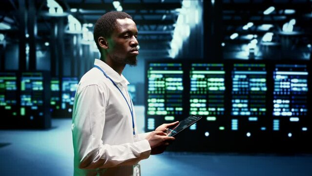 Electrician inspecting server racks delivering web content to customers over the internet. African american wireman using tablet to take note of critical systems, looking for potential errors