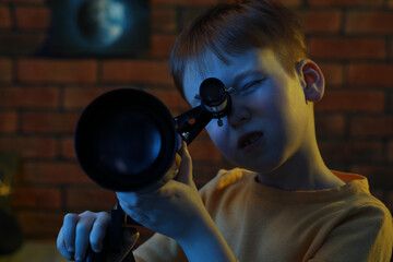 Little boy looking at stars through telescope in room