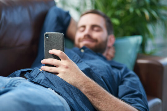 Nothing says self service like smart apps. Shot of a young man using a smartphone while relaxing on a sofa.