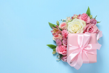 Gift box and beautiful flowers on light blue background, flat lay. Space for text