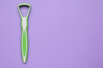 Green tongue cleaner on violet background, top view. Space for text