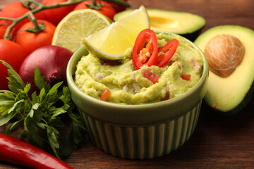 Bowl of delicious guacamole and ingredients on wooden table, closeup