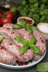 Raw homemade sausages, basil leaves and peppercorns on grey table, closeup