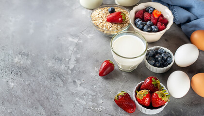 Organic ingredients for healthy breakfast - berries, milk, egg, oatmeal on grey concrete background. Copy space. Healthy food concept. Banner