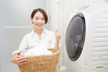 洗濯機の前で洗濯物を持ってグッドポーズするミドルエイジの女性