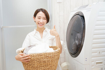 洗濯機の前で洗濯物を持ってグッドポーズするミドルエイジの女性