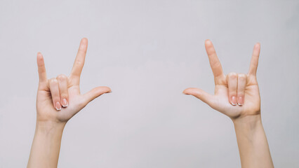 Rock sign. Punk gesture. Woman fingers showing horns symbols isolated on gray free space background.