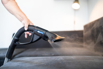 Cleaning service company employee removing dirt from furniture in flat with professional equipment. Female housekeeper arm cleaning sofa with washing vacuum cleaner close up. High quality photo