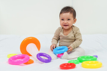 infant baby playing the pyramid toy with colored rings on bed