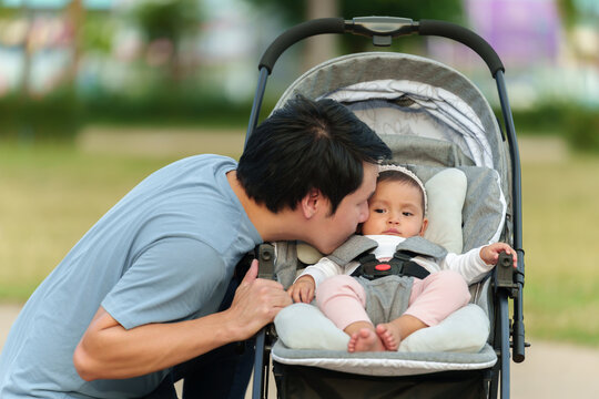 father kissing with his infant baby in the stroller while resting in the park
