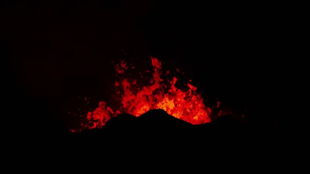 Night time volcano eruption with hot molten magma spewing from crater