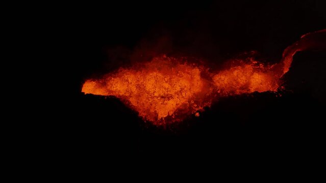Top down of orange glowing lava exploding from volcano crater at night, Iceland