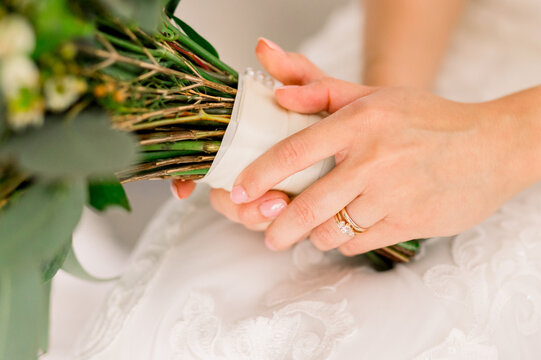 A bride holds her wedding bouquet and shows off her engagement ring and newly painted nails.