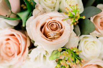 An engagement ring and wedding band set is inside a pink rose wedding bouquet. 