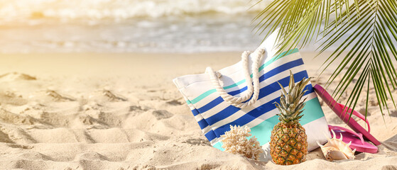 Beach bag with flip-flops and pineapple on sand near sea. Banner for design