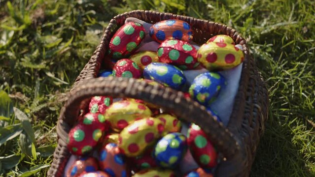 Close up shot of colorful Easter eggs in a basket on grass on a sunny day.