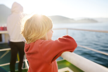 Blond little child is traveling with family by ferry or ship. Schoolboy is admiring the landscape of the Adriatic Sea. Cruise during the holidays.