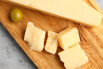 Wooden board with pieces of tasty Parmesan cheese on grunge background, closeup