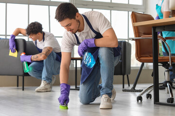 Male janitor cleaning floor with brush in office