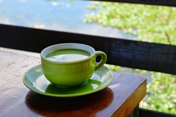 a cup of milk green tea on the table beside lake. the addition of milk to green tea may help mitigate the potential bitterness or astringency of some green teas, making it more enjoyable.