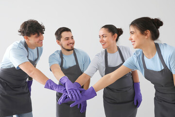 Young janitors putting hands together on grey background